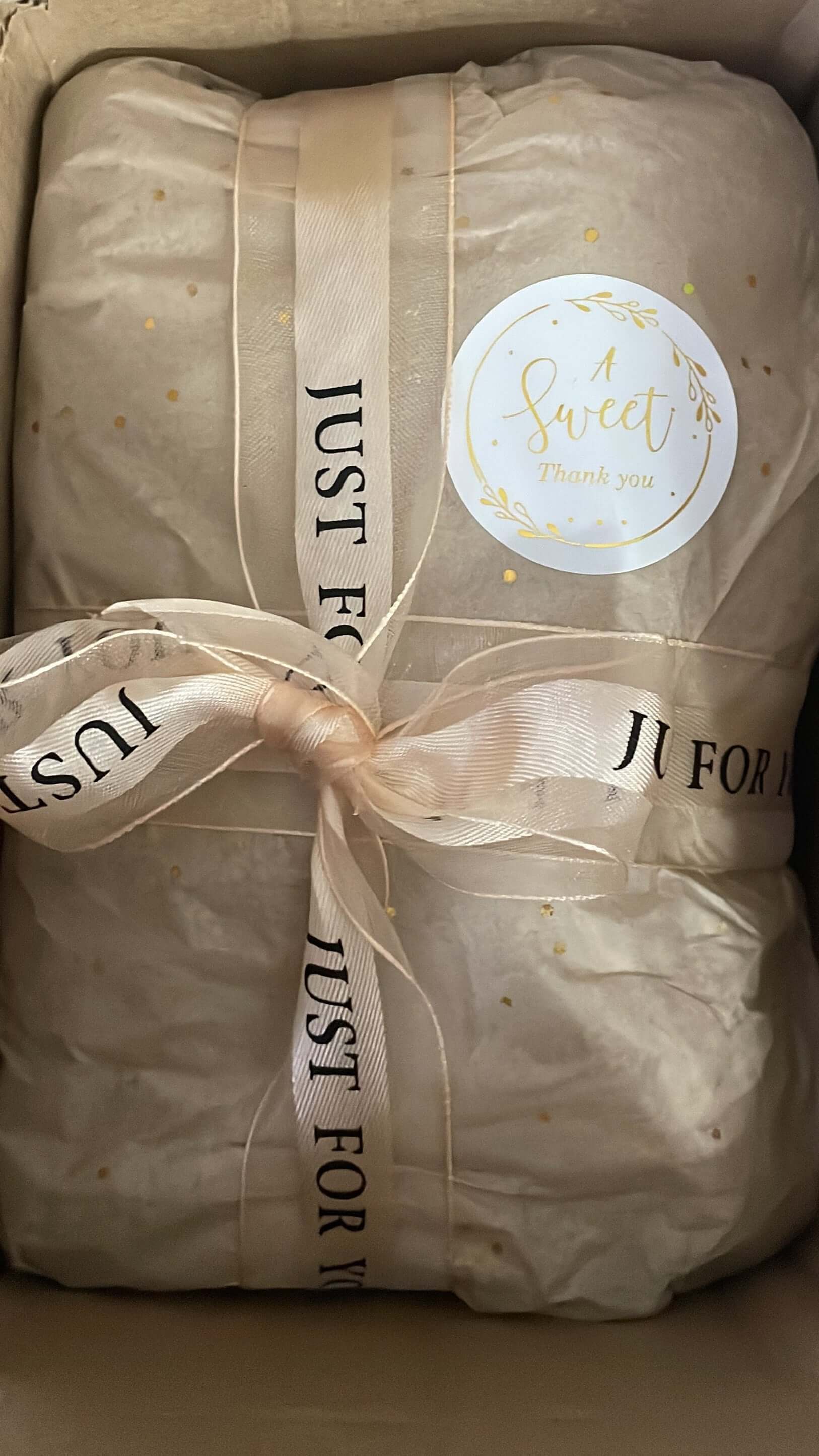 Product wrapped in beige paper with a ribbon and decorative label, sitting on a brown surface.